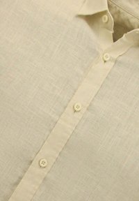 Beige linnen overhemd met een spitse kraag, voorzien van zeven kleine knopen langs de voorplacket en een gestructureerde stofafwerking.