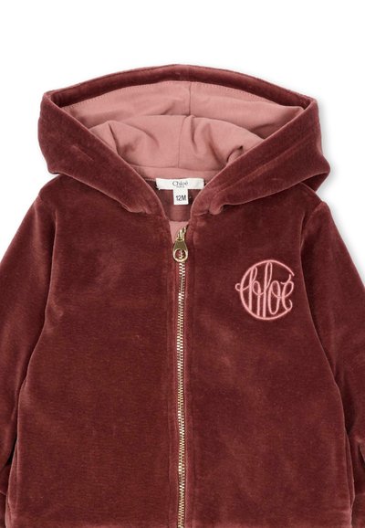 Bordowa welurowa bluza z kapturem na zamek błyskawiczny z różowym wnętrzem, z delikatnie wyhaftowanym logo. Miękka faktura, przedni zamek oraz design z kapturem.