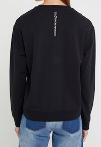 Sudadera negra de algodón con corte relajado, presenta un escote redondo y un sutil detalle del logo impreso verticalmente en la parte posterior.