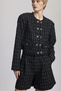 Black tweed jacket with white check pattern, fringe detailing, and silver buttons. Paired with matching tweed shorts, featuring pleats.