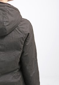 Dark olive green hooded jacket, featuring a matte finish, slightly wrinkled texture, and stitched detail along the seams.