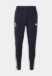 Pantalones deportivos de color marino con cintura elástica, que cuentan con el logo blanco de Adidas y el escudo del Real Madrid, acentuados con franjas laterales en amarillo y gris.