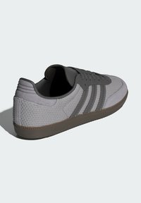 Grå sportskor med en texturerad mesh-oversida, släta överlägg och tre mörkgrå ränder. Gummisulor för bra grepp.