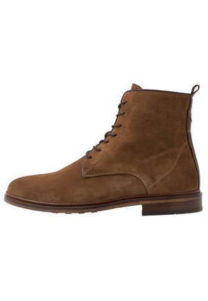 Bottine en cuir suédé marron avec des lacets marron foncé, languette à l’arrière et semelle en bois superposée, vue de l'extérieur.