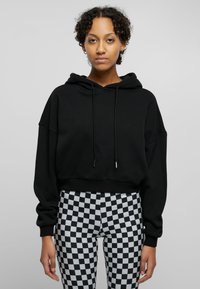 Svart cropped hoodie med snøring, med løse ermer. Kombinert med svart og hvitt rutete leggings, som fremhever kontrasterende mønstre.