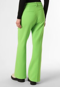 Rozšířené, jasně zelené kalhoty z pevných tkanin, s zadními kapsami a nošeny s platformovými botami, zobrazeno z zadního úhlu.