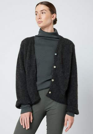 Dark gray wool cardigan with a loose fit, featuring ribbed cuffs, a button closure, and a soft texture, layered over a dark green turtleneck.