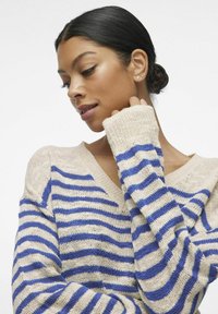 Pull rayé beige et bleu, avec un col en V et des manches longues à poignets côtelés. La texture tricotée est légère et respirante.