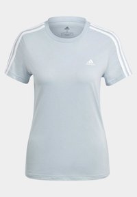 Gaiši zils īsās piedurknes T-krekls, kas izgatavots no gludas auduma. Tam ir trīs baltas svītras uz pleciem un neliels balts logo uz krūtīm.