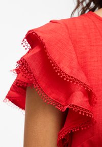 Manche en tissu rouge avec des volants superposés bordés d'une garniture dentelle sur le bras et l'épaule d'une personne.