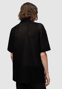Maglietta nera a maniche corte con vestibilità ampia, realizzata in un tessuto a rete testurizzato, caratterizzata da un collo largo e un design semplice.