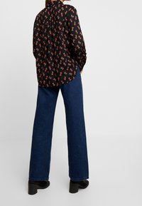 Camisa negra de botones con estampado animal en rojo y naranja; combinada con jeans de mezclilla oscura de pierna ancha y botas de tacón negras.