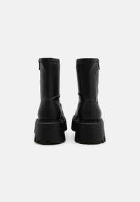 Bottines en cuir noir avec une semelle épaisse, dotées d'une fermeture éclair à l'arrière et d'une couture contrastante le long du bord supérieur.