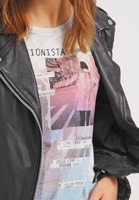Black leather motorcycle jacket over a light gray t-shirt featuring a graphic print with text and a street scene in pastel colors.