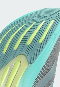 Suola della scarpa con una superficie grigia texturizzata e accenti turchesi e giallo neon. Scanalature e motivi evidenti per la trazione.