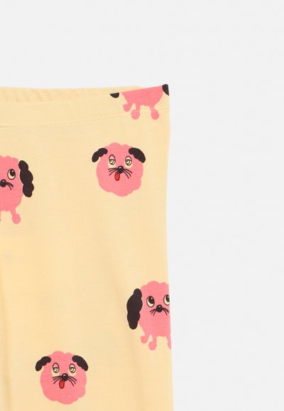 Žlutá látka s opakujícím se růžovým kresleným psem s černýma ušima a výraznýma očima na hladkém textilním povrchu.