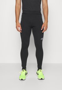 Leggings sportivi neri con un design aderente, realizzati in tessuto elasticizzato, caratterizzati da un logo sul lato sinistro e indossati con sneaker verde neon.