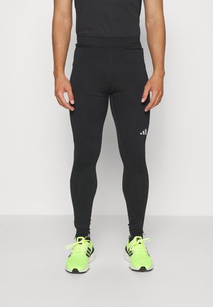 Black athletic leggings with a fitted design, made of stretchy fabric, featuring a logo on the left side and worn with neon green sneakers.