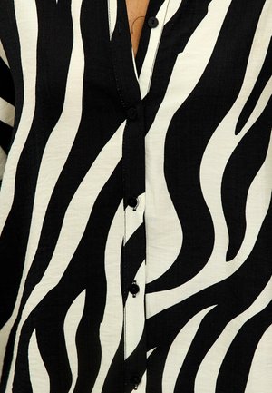 Chemise à manches longues à motif zèbre noir et blanc avec un tissu texturé, présentant de grands motifs ondulés et des boutons noirs sur le devant.