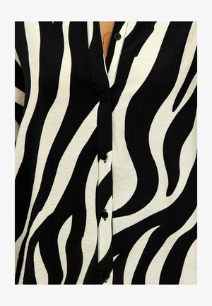 Chemise à manches longues à motif zèbre noir et blanc avec un tissu texturé, présentant de grands motifs ondulés et des boutons noirs sur le devant.