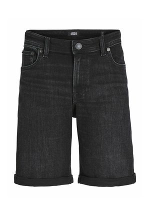 Person iført en grå hættetrøje med teksten "JACK & JONES", sorte opkrøllede denimbukser, sorte sokker og hvide sneakers, stående mod en ensfarvet baggrund.