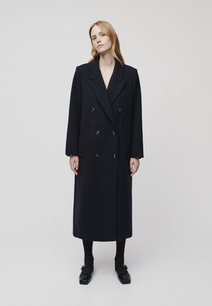 Dark navy double-breasted wool coat with large lapels, front pockets, and black buttons. Mid-calf length, straight silhouette, and long sleeves.