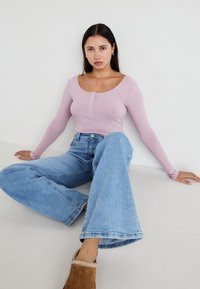 Lys lavendel ribbet langermet topp med knapppreg, paret med høytlivs lyseblå vide jeans og brune pelsforede sko.