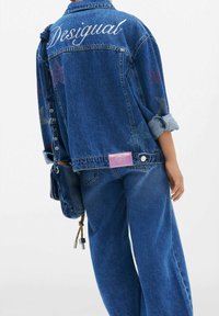 Džínová bunda svetlo modrej farby, so vyšívaným nápisom "Desigual" a hviezdičkovými vzormi s malými nitmi na zadnej strane. Veľký strih.