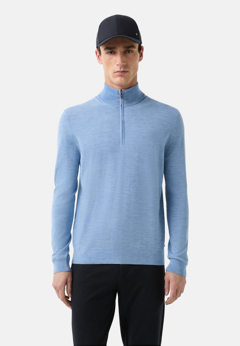 Hellblauer Zip-Up-Pullover aus weichem Strickstoff, mit hohem Kragen und langen Ärmeln, kombiniert mit dunklen Hosen.