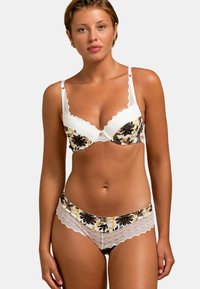 Soutien-gorge à dentelle et culottes assorties en imprimé floral. Couleurs blanche, noire et jaune avec des bords festonnés et des boutons décoratifs.
