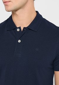 Mornarsko polo majica iz teksturiranega blaga, z klasikim ovratnikom, dvema belima gumboma in majhnim izvezenim logotipom na prsih.