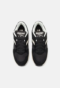 Black sneakers feature a mesh and suede upper, round laces, padded collar, and a white logo on the tongue. Textured rubber outsole.