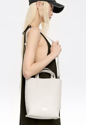 Geverfde witte leren tote bag met twee korte handvaten en een lange verstelbare schouderband, met een minimalistisch ontwerp en subtiele branding.