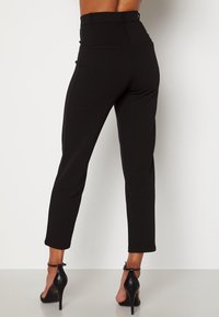 Pantalon noir taille haute en tissu extensible, avec deux poches arrière et une coupe slim, se terminant juste au-dessus de la cheville.