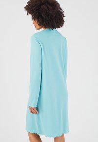 Robe à manches longues en tissu côtelé bleu clair avec des détails en bordure festonnée à l'ourlet et aux poignets. Coupe décontractée, longueur genou, texture lisse.