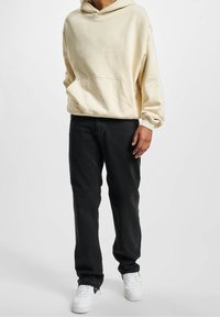 Kremowy sweatshirt z kapturem ma przednią kieszeń. W połączeniu z czarnymi spodniami i białymi sneakersami tworzy casualowy wygląd.