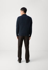 Maglione a coste blu navy con colletto alto, abbinato a pantaloni marrone scuro e scarpe nere. Il capo presenta un design a maglia testurizzata.