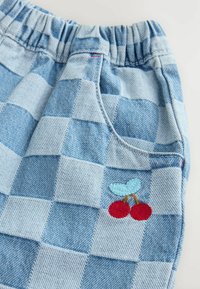 Világoskék kockás farmernadrág rövidnadrág, gumis derékkal, amelynek elülső zsebében hímzett cseresznye minta található.