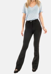 Pantalones acampanados negros de tela texturizada con bolsillos frontales, combinados con una camiseta de cuello en v azul claro. Calzado negro completa el conjunto.