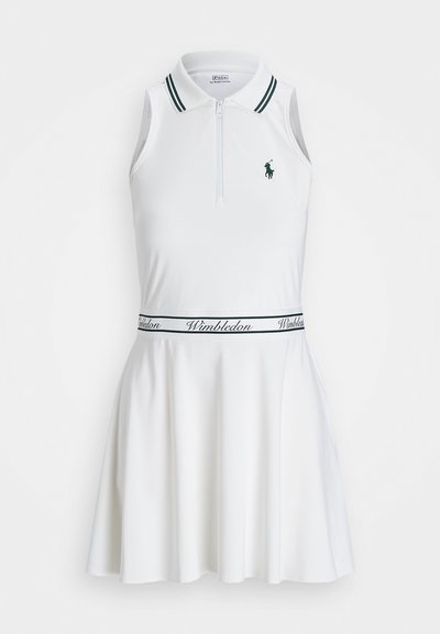 Balta be rankovių suknelė su polo apykakle, užtrauktuku ir žaliais akcentais; turi kontrastingą Vimbldono logotipo juostą ties liemeniu.