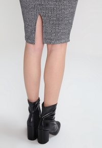 Szara prążkowana spódnica z tylnym rozcięciem, zestawiona z czarnymi błyszczącymi botkami na kostkę z masywnym obcasem. Materiał jest miękki i dopasowany.