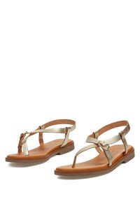Sandalias metálicas doradas con un diseño de tira en T y suelas de color marrón claro, que cuentan con una hebilla decorativa en el lateral.