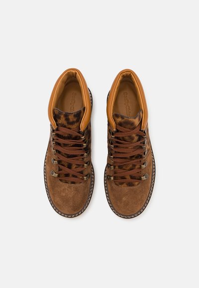 Zapatos de ante marrón con un cuello de tobillo de cuero, cordones marrones y una parte superior de tejido estampado. Incluye ojales de metal y costuras en contraste.