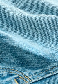 Pânza de denim albastru deschis, cu o țesătură texturată, având cusături vizibile de culoare galbenă contrastantă pe margine.
