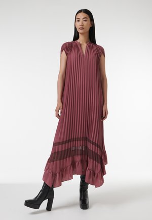 Fließendes, plissiertes Kleid in Mauve mit kurzen Ärmeln, einem Schlüssellochausschnitt und einem transparenten, rüschierten Saum. Kombiniert mit schwarzen Plateau-Stiefeln.