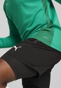 Groen sporttop met contrasterend mesh paneel, gecombineerd met zwarte shorts met een wit logo en DRYCELL-details. Soepel, aansluitend ontwerp.