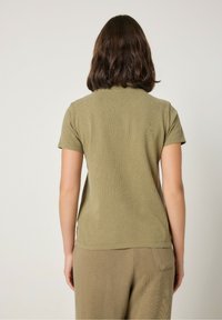 Olivovo zelené tričko s krátkymi rukávmi a štruktúrovanou tkaninou, s okrúhlym výstrihom a voľným strihom, skombinované s béžovými nohavicami.