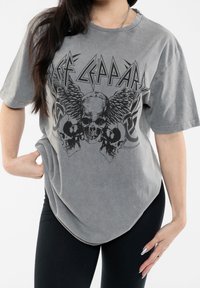 Gray oversized t-shirt made of soft fabric features a distressed print of a skull with wings and band name in bold lettering.
