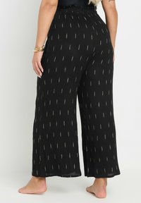 Mustat leveät housut, joissa on hierottu kangas, jossa on kullanlehden kuvioita ja joustava vyötärö mukavuutta varten.