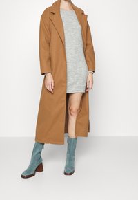 Brązowy długi płaszcz z mieszanki wełny, szara dzianinowa sukienka oraz tealistoniebieskie zamszowe botki na kostkę z drewnianym obcasem.